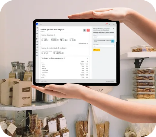 Comerciante segurando um tablet com o painel financeiro do ConnectStore aberto, ao lado das prateleiras da loja